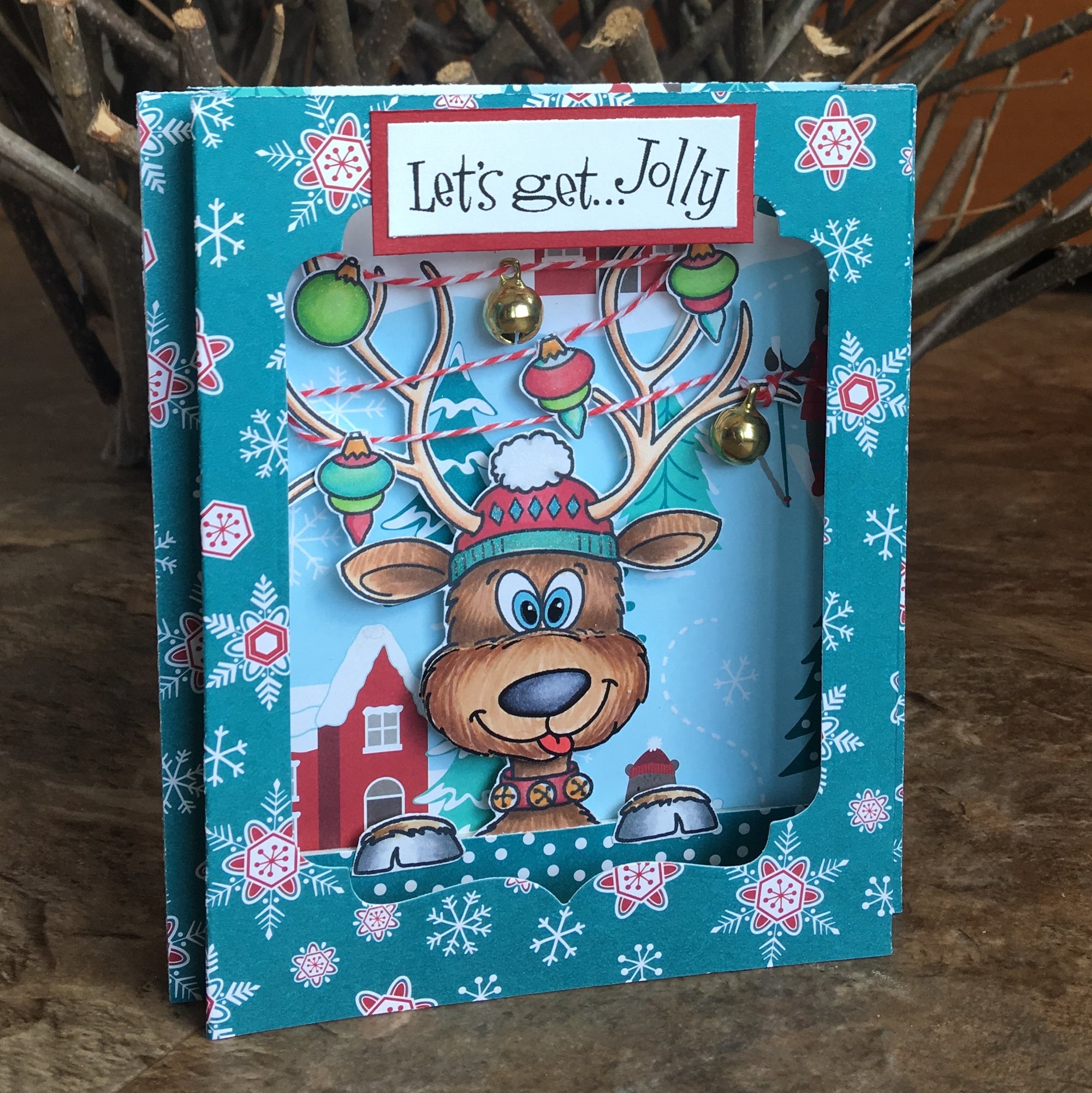 Handmade card with a silly reindeer and ornaments hanging off the antlers with the sentiment, "Let's get jolly". Uses the stamp set and die cut, "Reindeer Games" from Dare 2B Artzy.